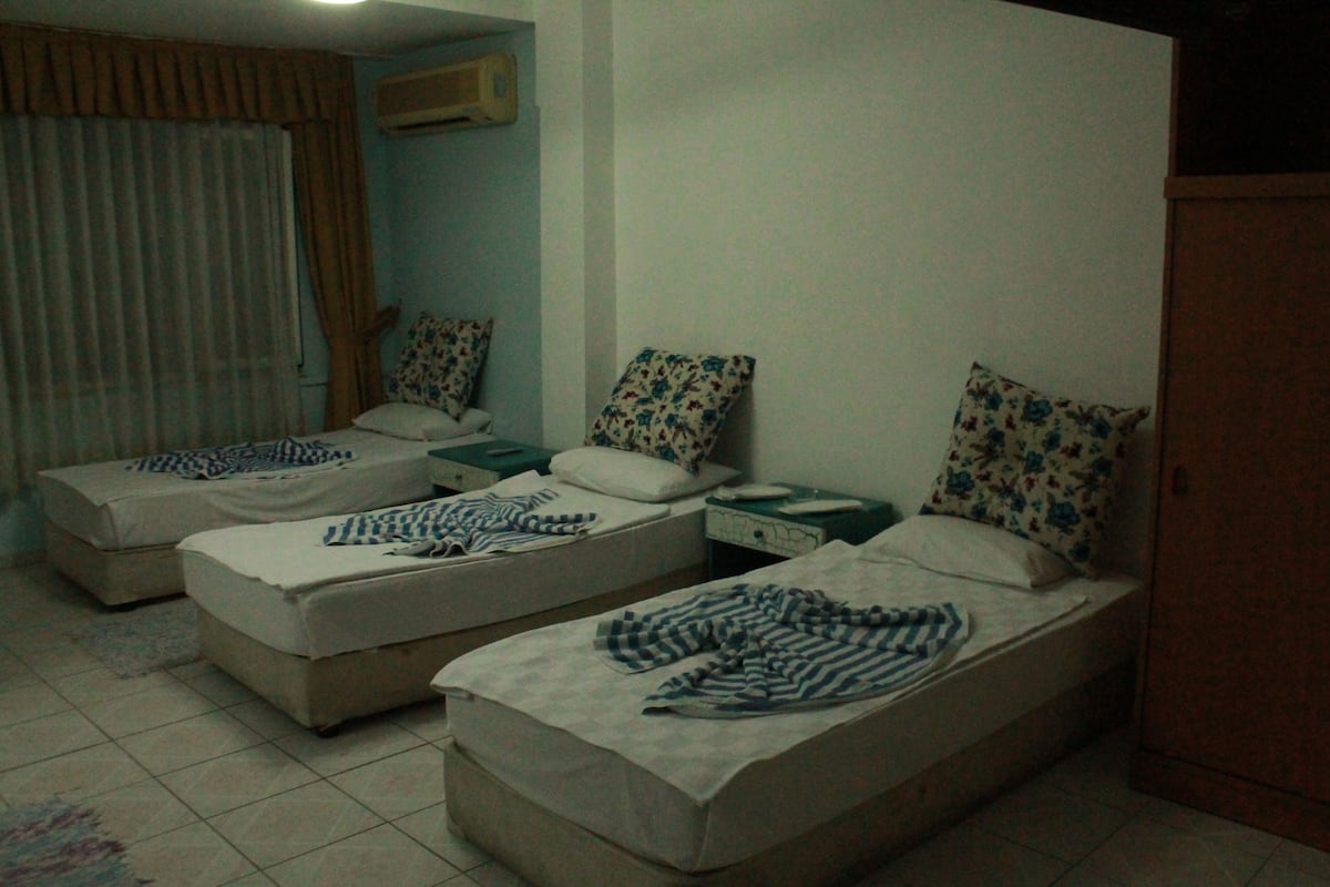 A small, dimly lit room with two single beds, each with a floral pillow and a striped blanket.