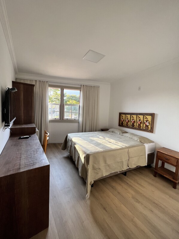 Un dormitorio con cama, escritorio, silla, ventana con cortinas y un marco de imagen colgado en la pared.