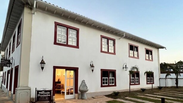 A two-story building with a white facade and red window frames. There is a sign in front that reads "Pet Shop." - Pousada Tiradentes (Tiradentes)