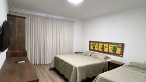 A hotel room with two beds, a wooden desk, a flat-screen TV mounted on the wall, and a ceiling light. - Pousada Tiradentes (Tiradentes)