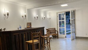 A reception area with a wooden counter, bar stools, wall-mounted light fixtures, and a glass door leading outside. - Pousada Tiradentes (Tiradentes)