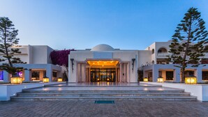 Une entrée d’hôtel moderne, avec un dôme central, des marches menant à l’entrée et des lanternes illuminées de part et d’autre.