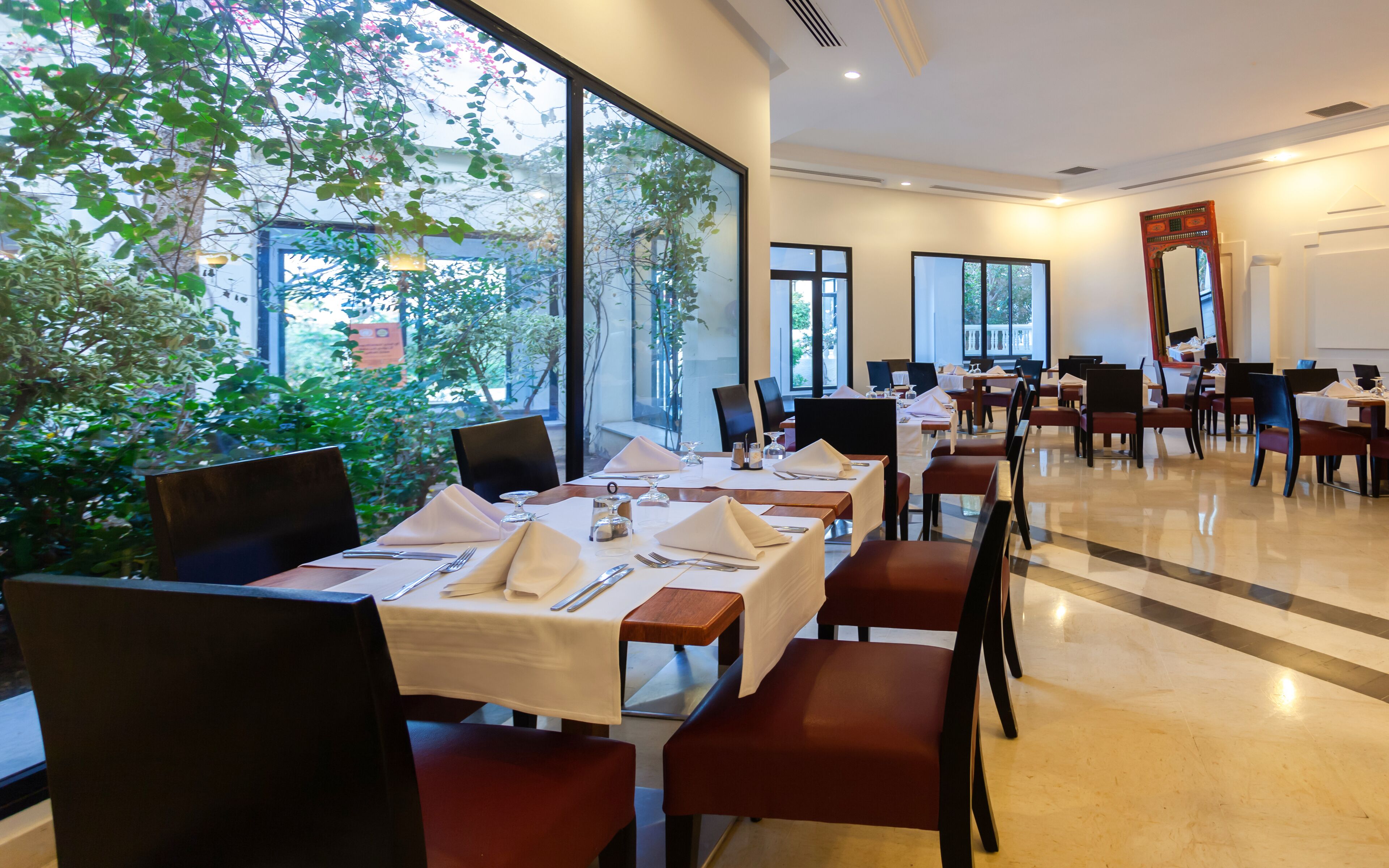 Ein Restaurant mit gedeckten Tischen, großen Fenstern mit Blick auf Grünflächen und einem hellen, modernen Innenraum.