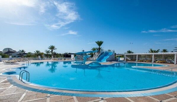 Una gran piscina con tobogán, sillas de descanso y palmeras.