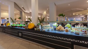 Un espace buffet proposant divers plats et décorations, notamment une grande citrouille jaune et plusieurs plantes en pot.