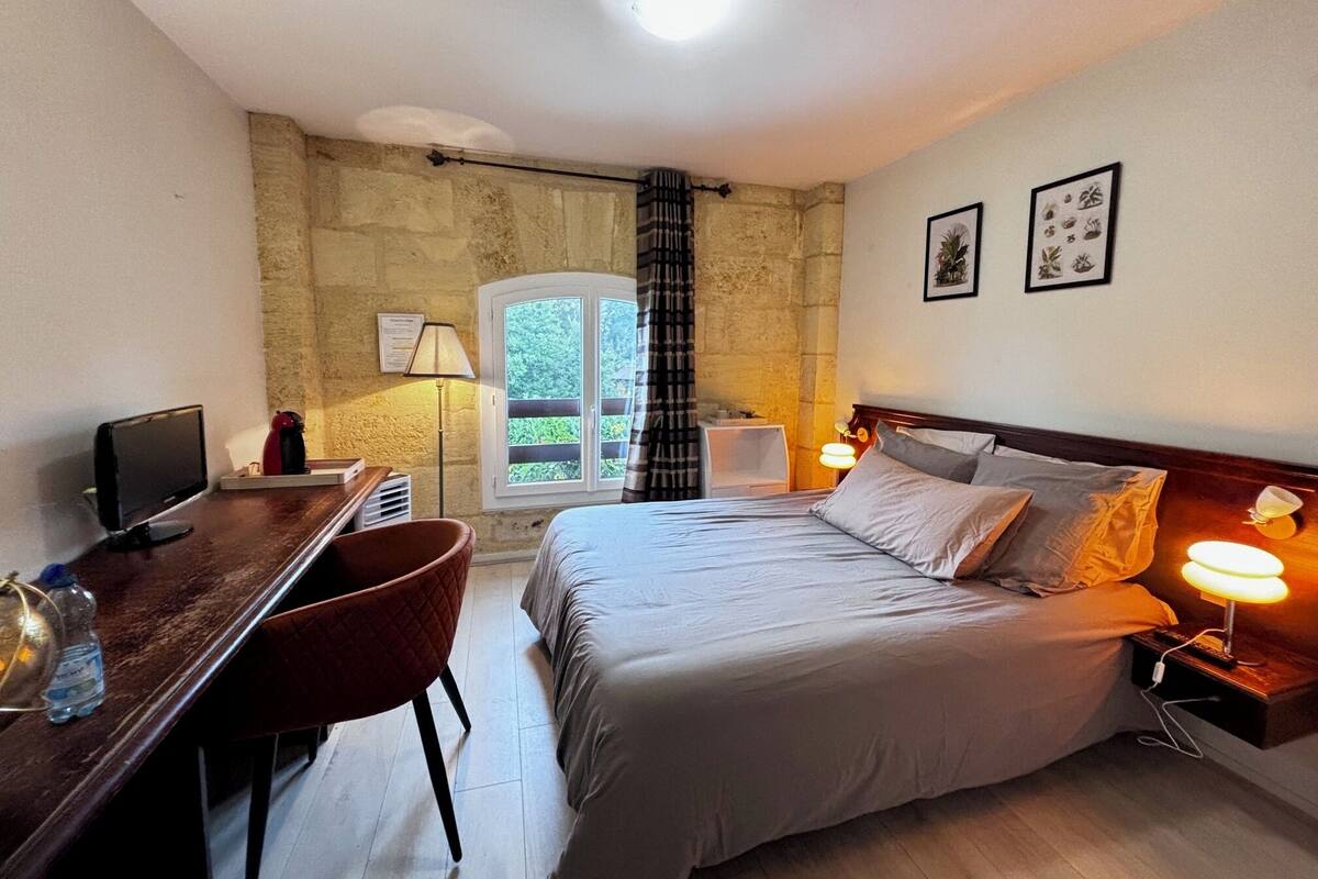 Habitación de hotel con cama, escritorio, silla y ventana con vistas al follaje.