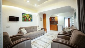 A modern living room with a sofa, armchairs, and a flat-screen TV. There is a kitchen in the background with wooden cabinets and a refrigerator. - Zeybek 2 Pension & Apart (Kas)