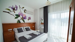 A modern hotel room with a large bed, a wooden headboard, a nightstand, a bedside table, and a large window with sheer curtains. - Zeybek 2 Pension & Apart (Kas)