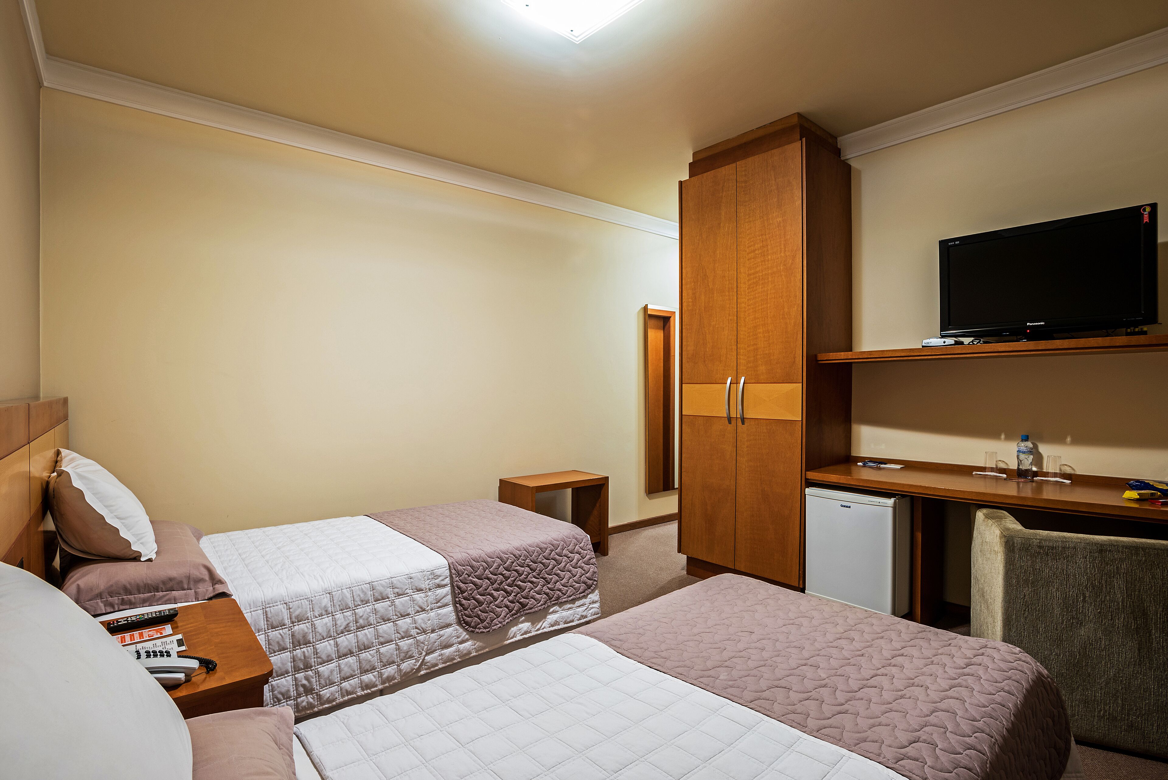 Une chambre d’hôtel avec deux lits, un bureau avec une télévision et un petit réfrigérateur.