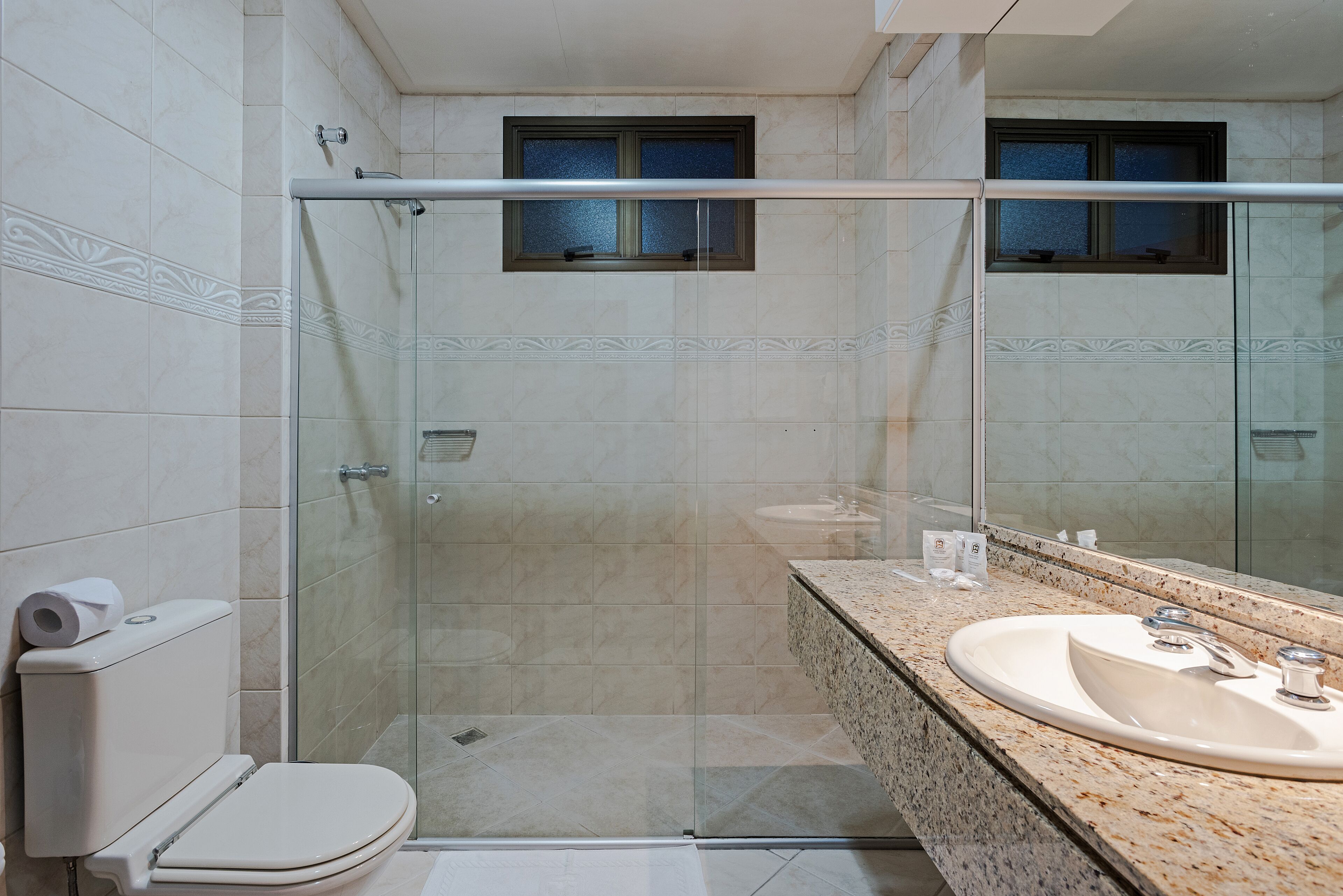 A modern bathroom with a glass-enclosed shower, a toilet, and a sink with a large mirror.