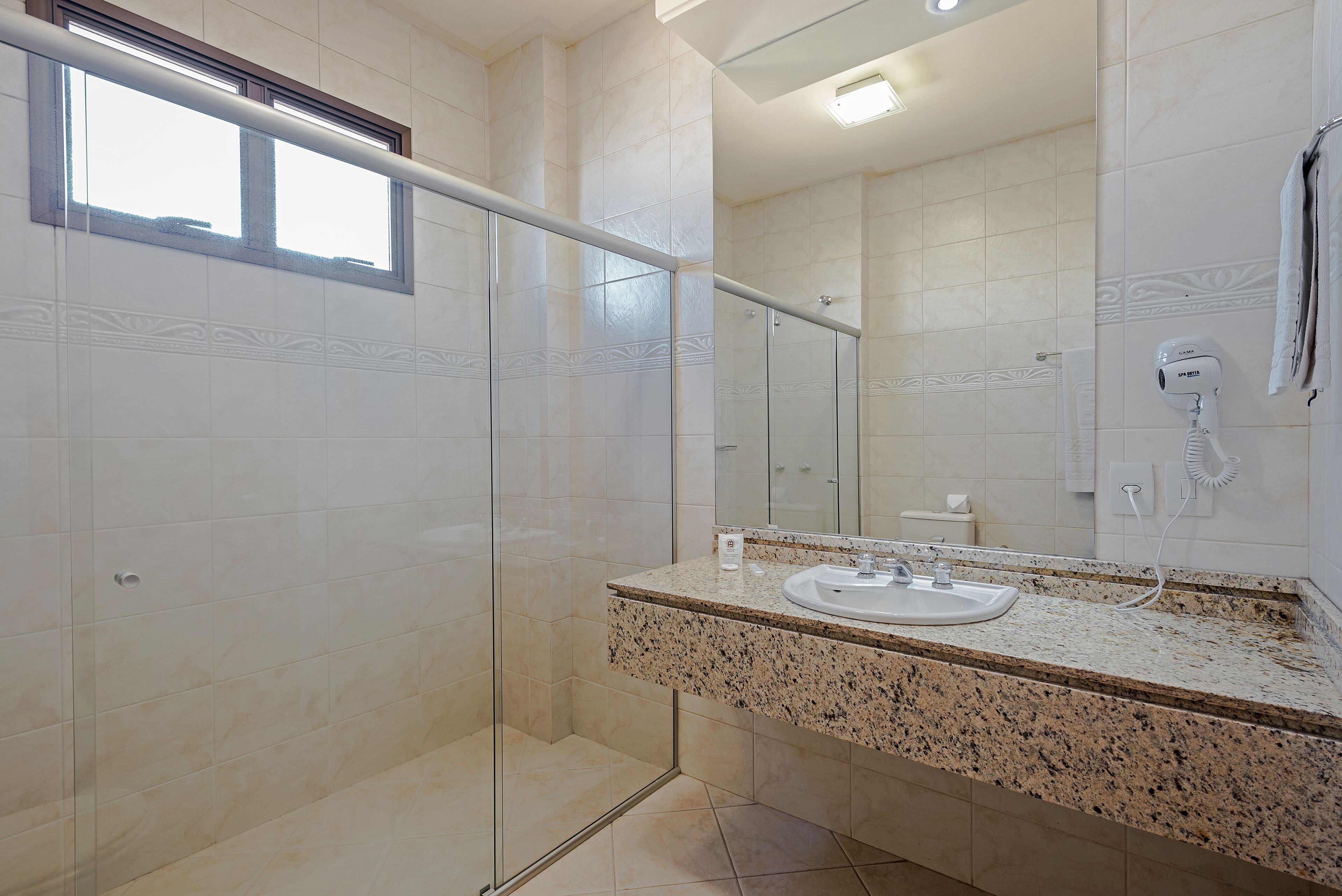 Un baño moderno con cabina de ducha de vidrio, encimera de granito y un espejo grande.