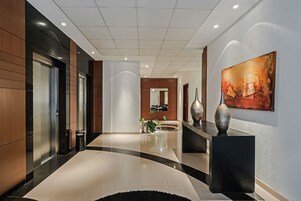 A modern hotel lobby with a curved black and beige floor, a reception desk, a large abstract painting, and a potted plant.