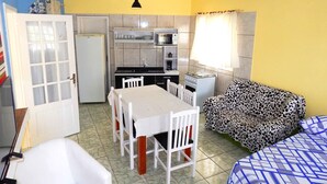 A compact kitchen with a dining table and chairs, a sofa, and a refrigerator.