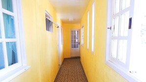 A narrow hallway with yellow walls, white-framed windows, and a tiled floor.