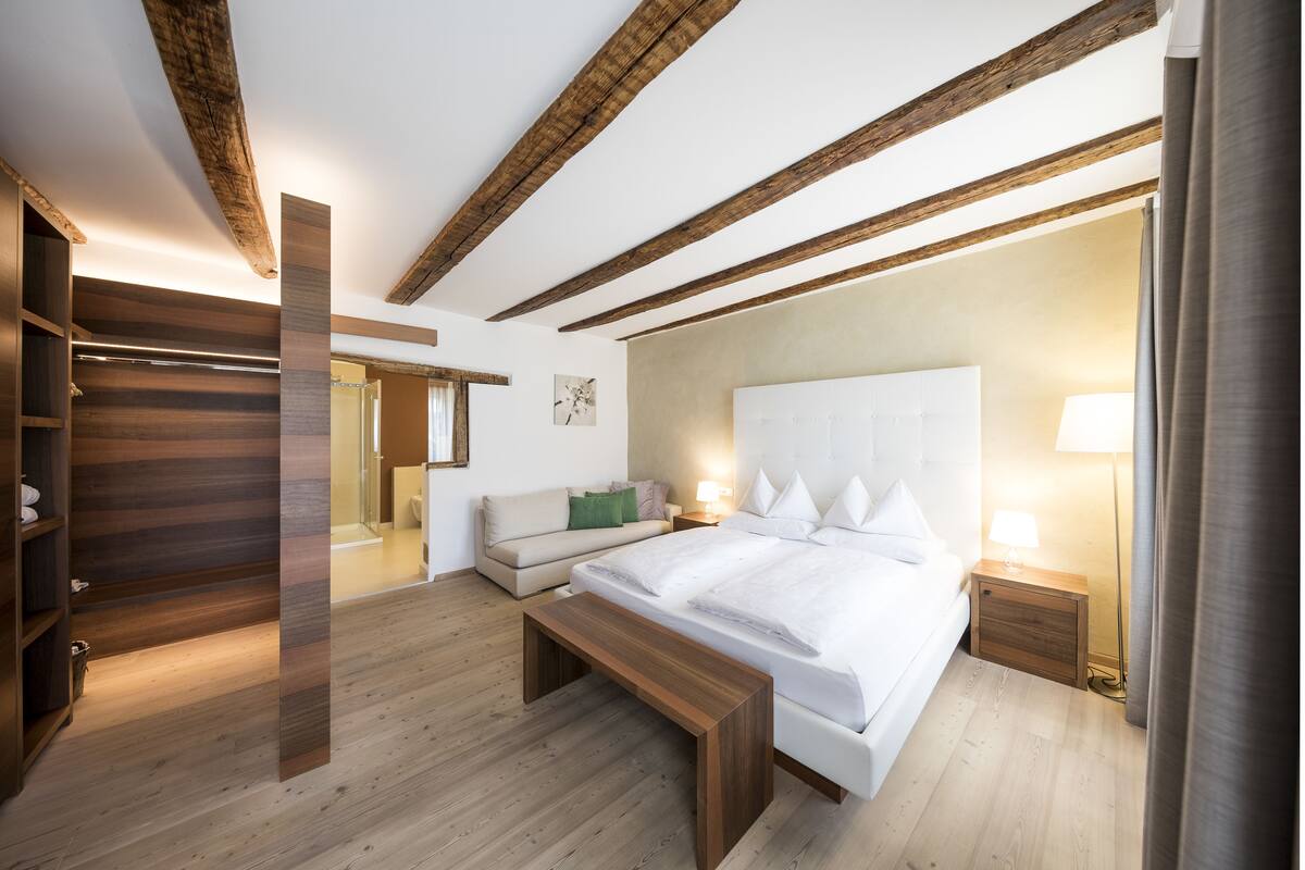 A modern bedroom with a large bed, wooden beams, a bench, a bedside table, and a nightstand.