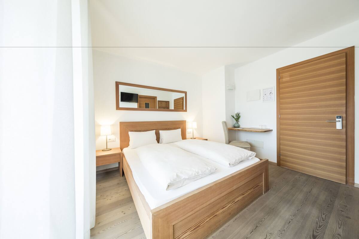 A modern bedroom with a wooden bed, bedside tables, a nightstand, a mirror, and a wooden wardrobe.