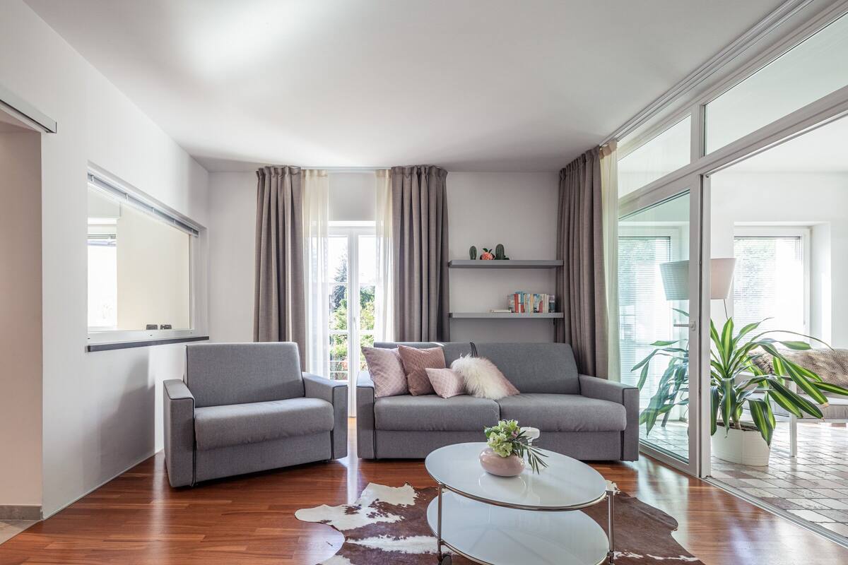 A modern living room with a grey sofa, a round coffee table, and a glass door leading to a balcony.