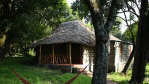 A rustic stone building with a thatched roof, surrounded by lush greenery and trees. - Mara Chui Resort (Maasai Mara)
