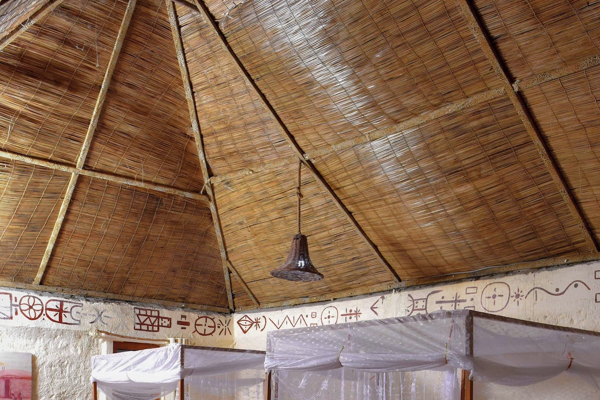 A traditional room with a thatched roof, two four-poster beds, a wooden table, and a chair.