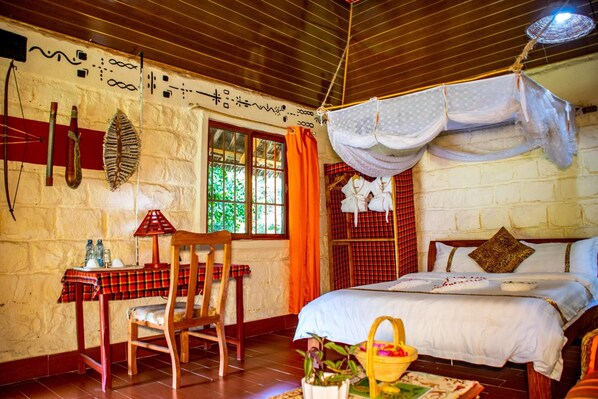 A room with a bed, a table with a red and black checkered tablecloth, a chair, a window with curtains, and a wall with decorative patterns.