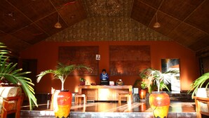 A reception area with a receptionist, wooden reception desk, potted plants, and a tiled floor. - Mara Chui Resort (Maasai Mara)