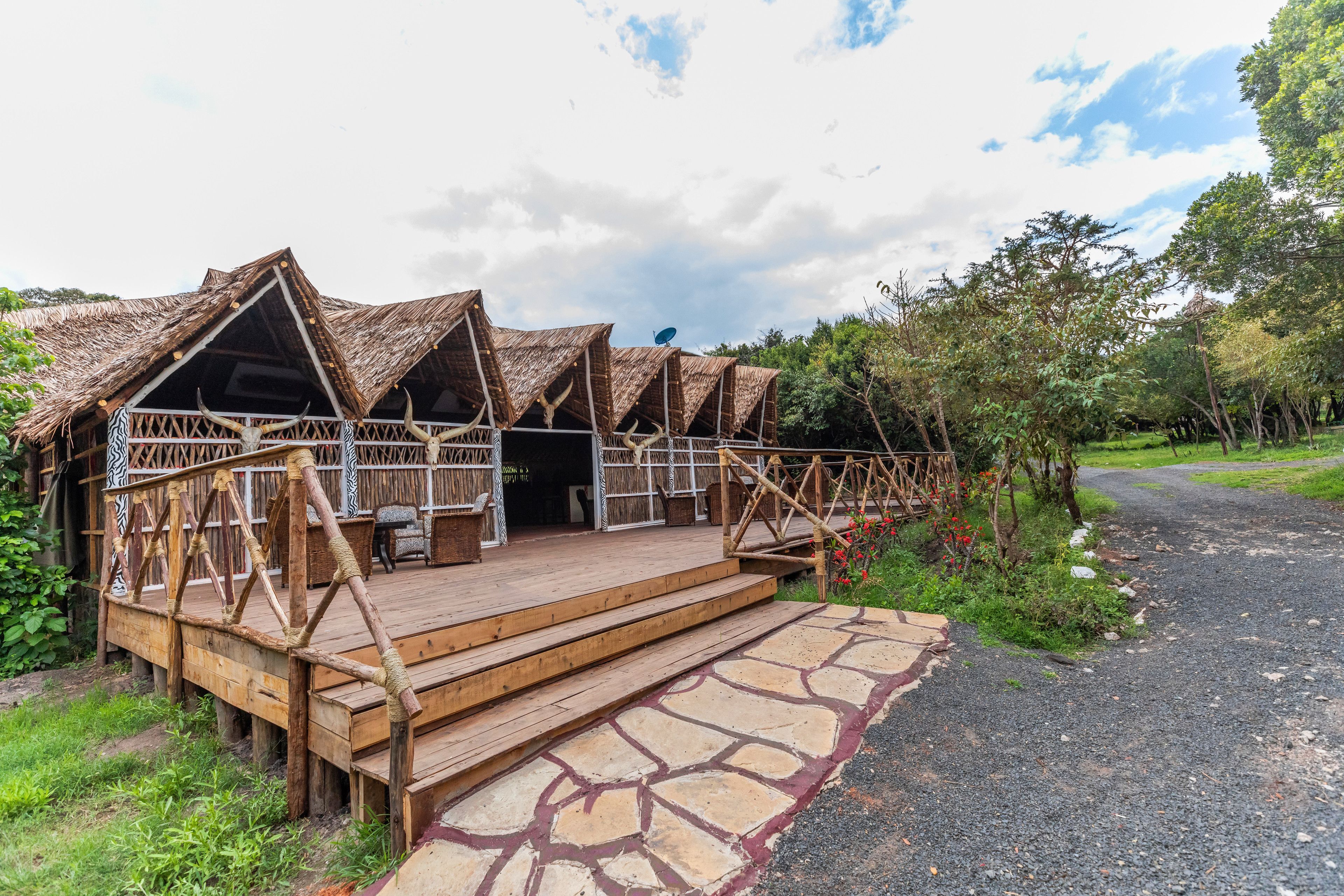 A rustic lodge with thatched-roof cabins, wooden deck, and a stone pathway leading to the entrance.