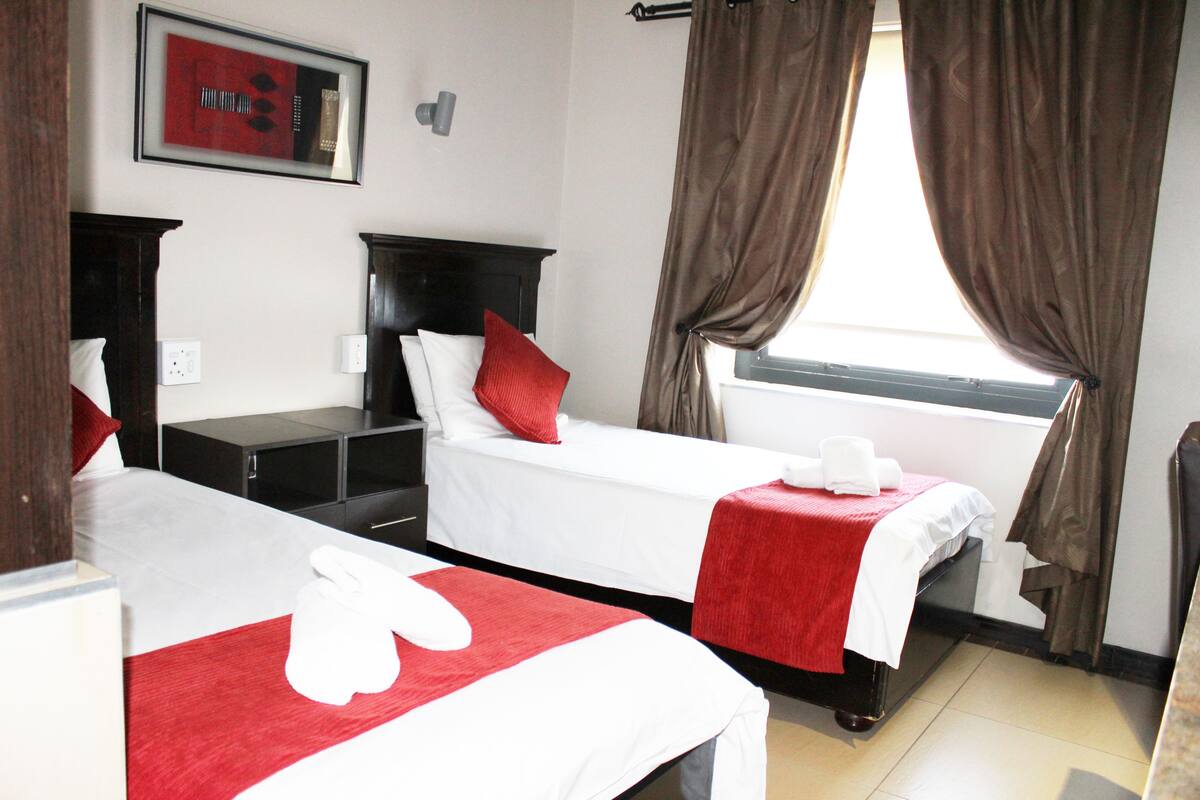 A hotel room with two beds, a nightstand, a dresser, a window with curtains, and a framed picture on the wall.