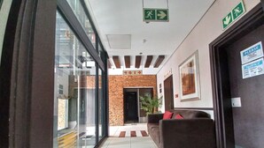 A hotel lobby with a reception desk, a brown sofa, a potted plant, and a glass wall. - Alcazaba Lodges (Johannesburg)