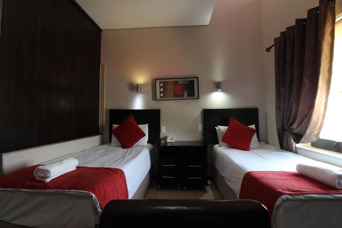 A hotel room with two beds, a desk, and a window with curtains.