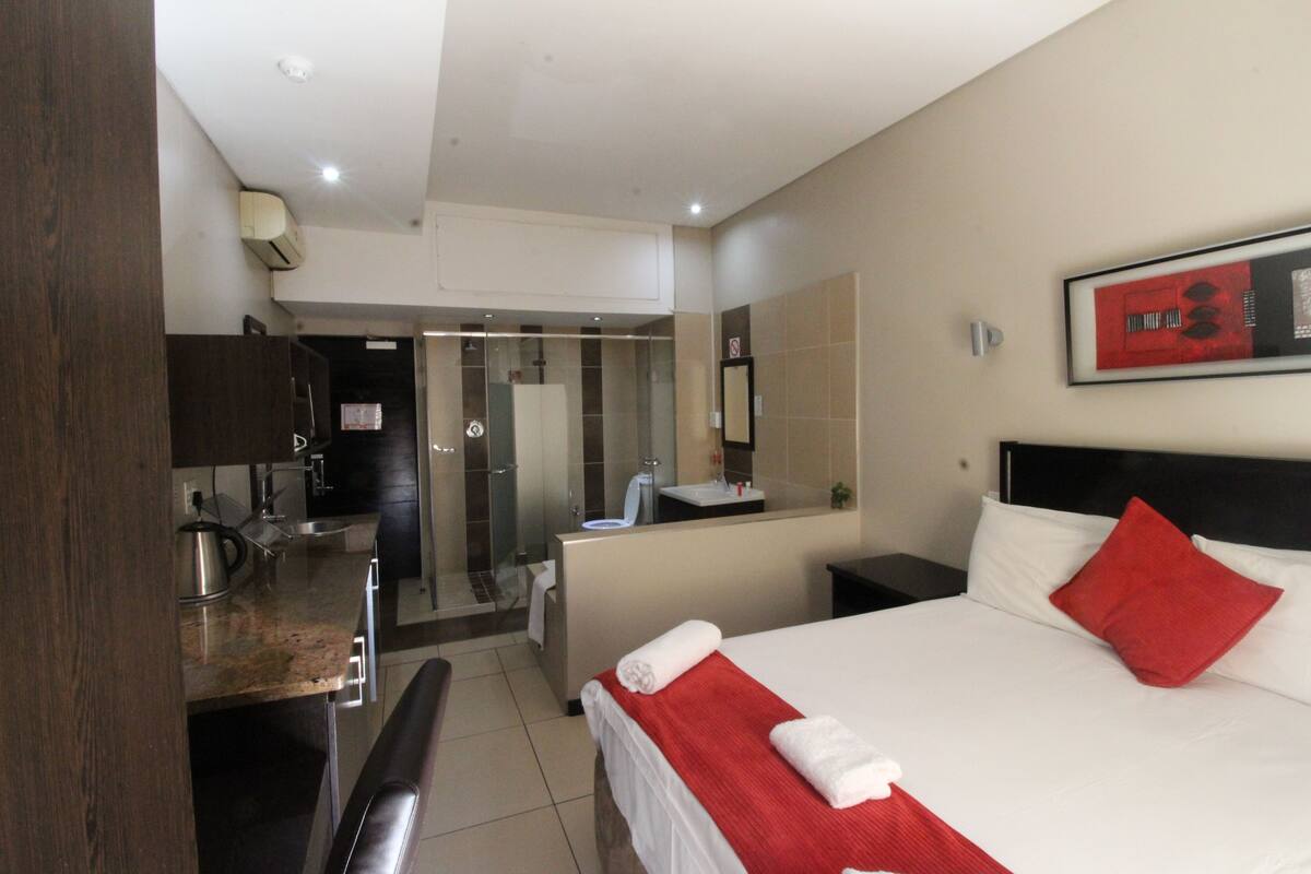A hotel room with a bed, a desk, a bathroom, and a shower area.