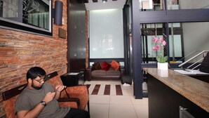 A modern interior with a brick wall, a seating area with a sofa and armchairs, a reception desk, and a large window. - Alcazaba Lodges (Johannesburg)