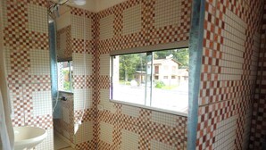 Un baño con paredes de baldosas a cuadros, una ventana, un lavamanos y un inodoro.