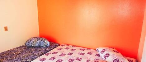A small, single-bed room with a red wall and a patterned bedspread.