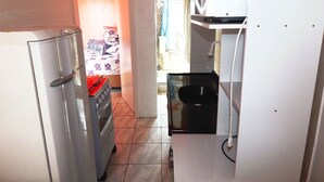 Cocina compacta con refrigerador, microondas y horno. Se ve un lavamanos pequeño y una puerta conduce a un dormitorio con cama y cortinas.