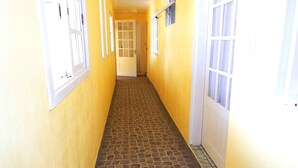 Un pasillo estrecho con paredes amarillas y piso de baldosas, que conduce a una puerta al final.