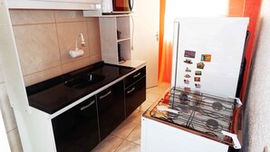 Una cocina compacta con encimera negra, armarios blancos, microondas, refrigerador y estufa a gas.