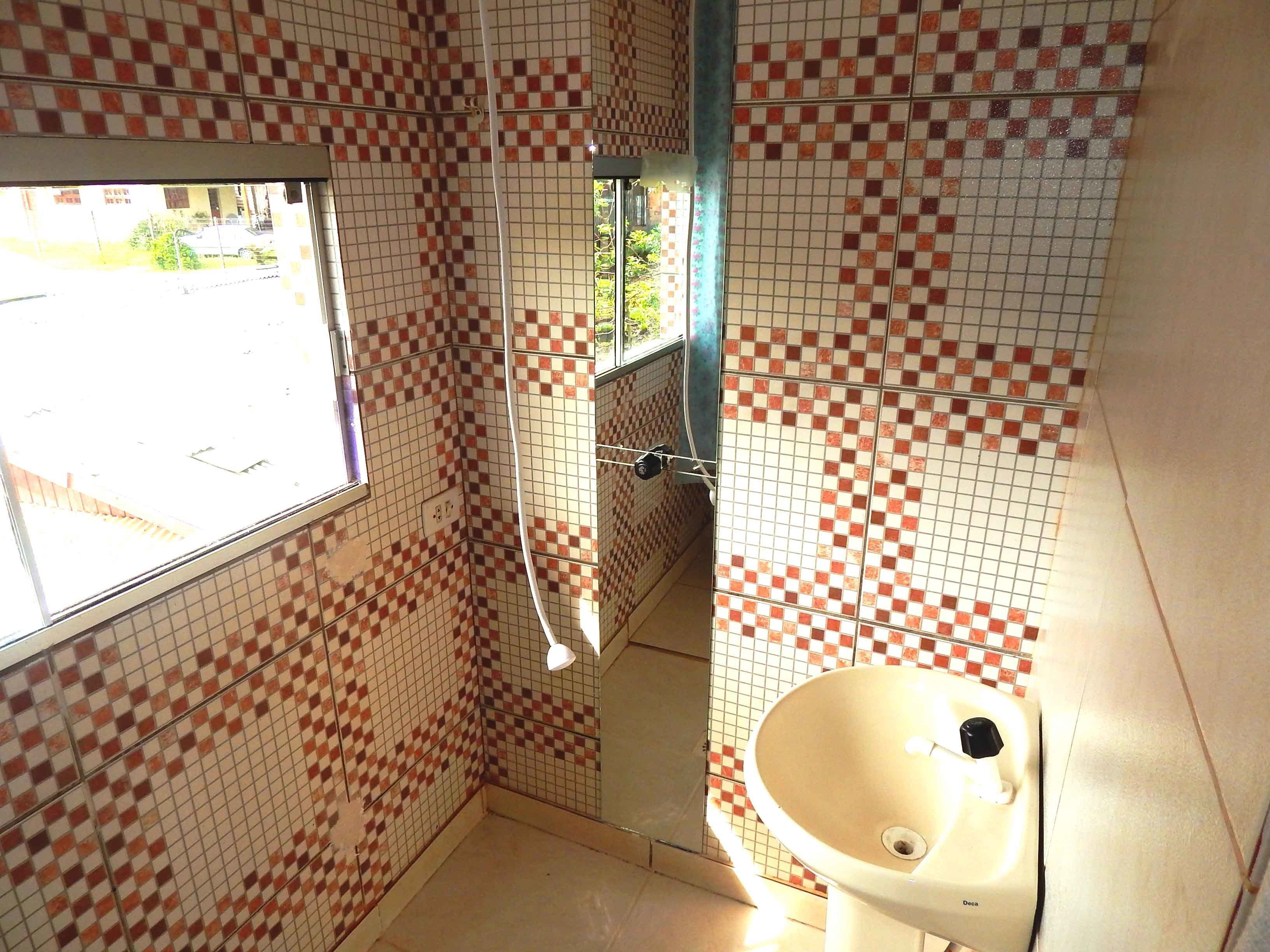 A bathroom with checkered tile walls, a window, a sink, and a shower.