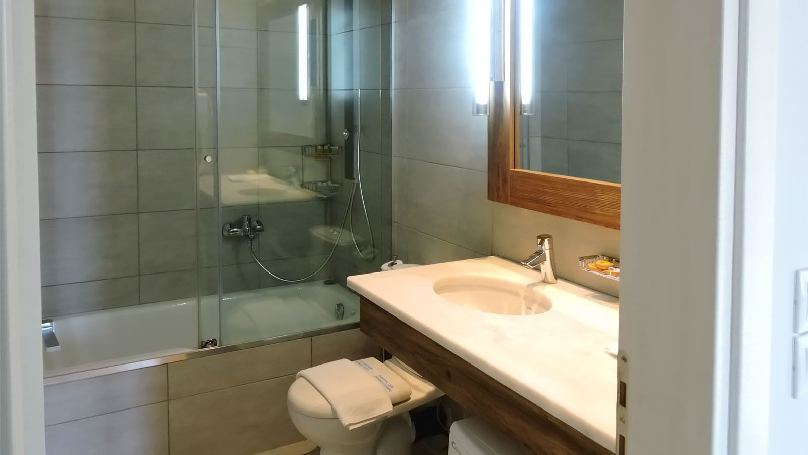 Ein modernes Badezimmer mit einer gläsernen Duschkabine, einem Waschbecken inklusive Spiegel und einer Toilette.