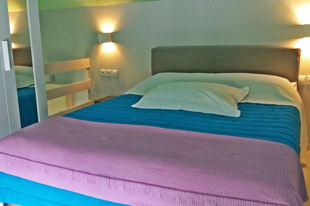 A bed with a blue and pink bedspread, a wooden headboard, and two wall-mounted lights.