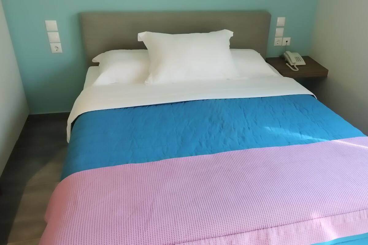 A bed with a blue and pink bedspread, a white pillow, and a bedside phone on a wooden nightstand.
