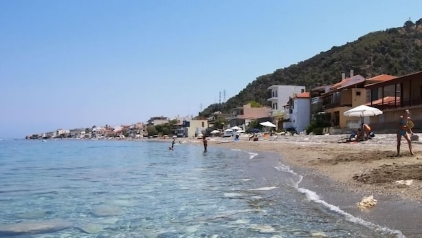 A beach with clear water, people swimming, and buildings along the shore. - Derveni Luxury Apartments  (Xylokastro-Evrostina)