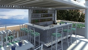 An outdoor bar area with a view of the sea, featuring a bar counter, seating with green cushioned chairs, and a wine rack with bottles. - Derveni Luxury Apartments  (Xylokastro-Evrostina)