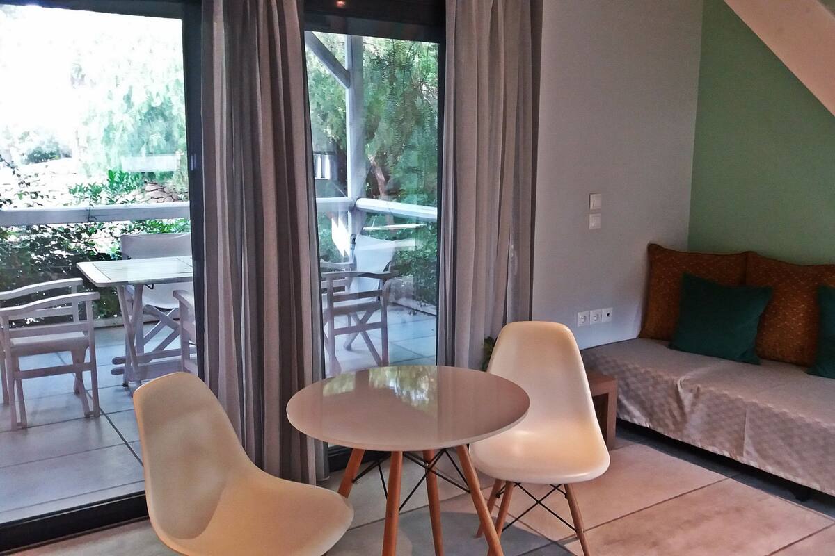 A modern living room with a sofa, two chairs, and a small table. There is a staircase leading to an upper level.