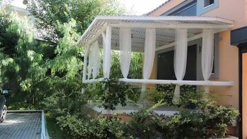 A covered outdoor area with a white structure, surrounded by greenery.
