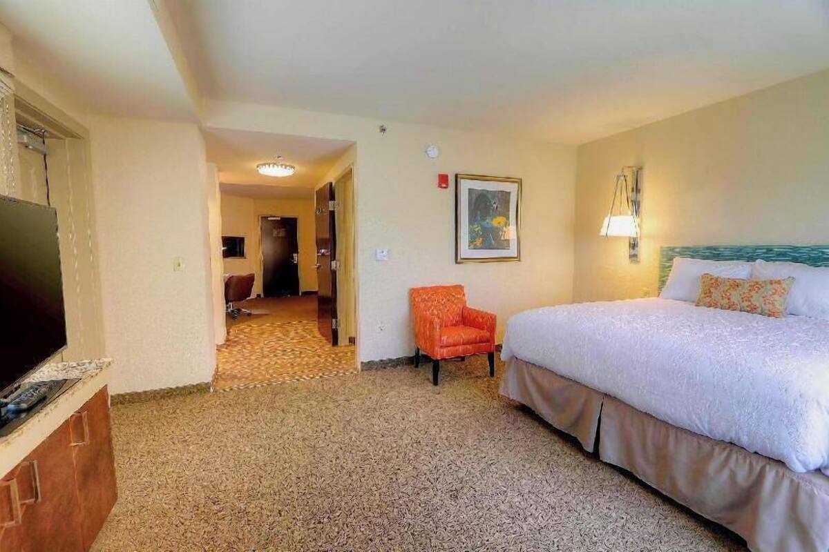 A hotel room with a bed, a television, a chair, and a painting on the wall.