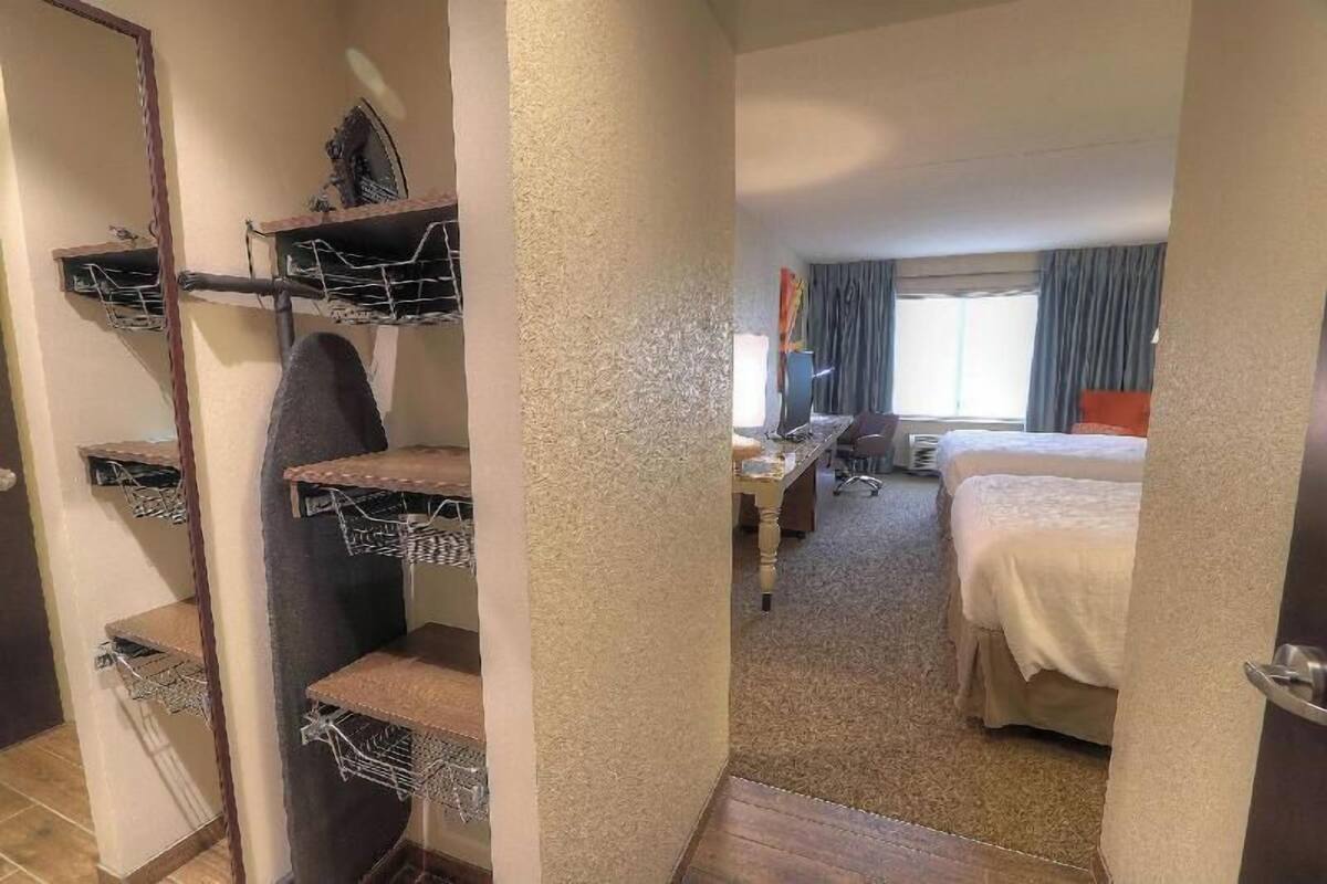 A hotel room with a bed, desk, chair, and a small kitchenette area with shelves.