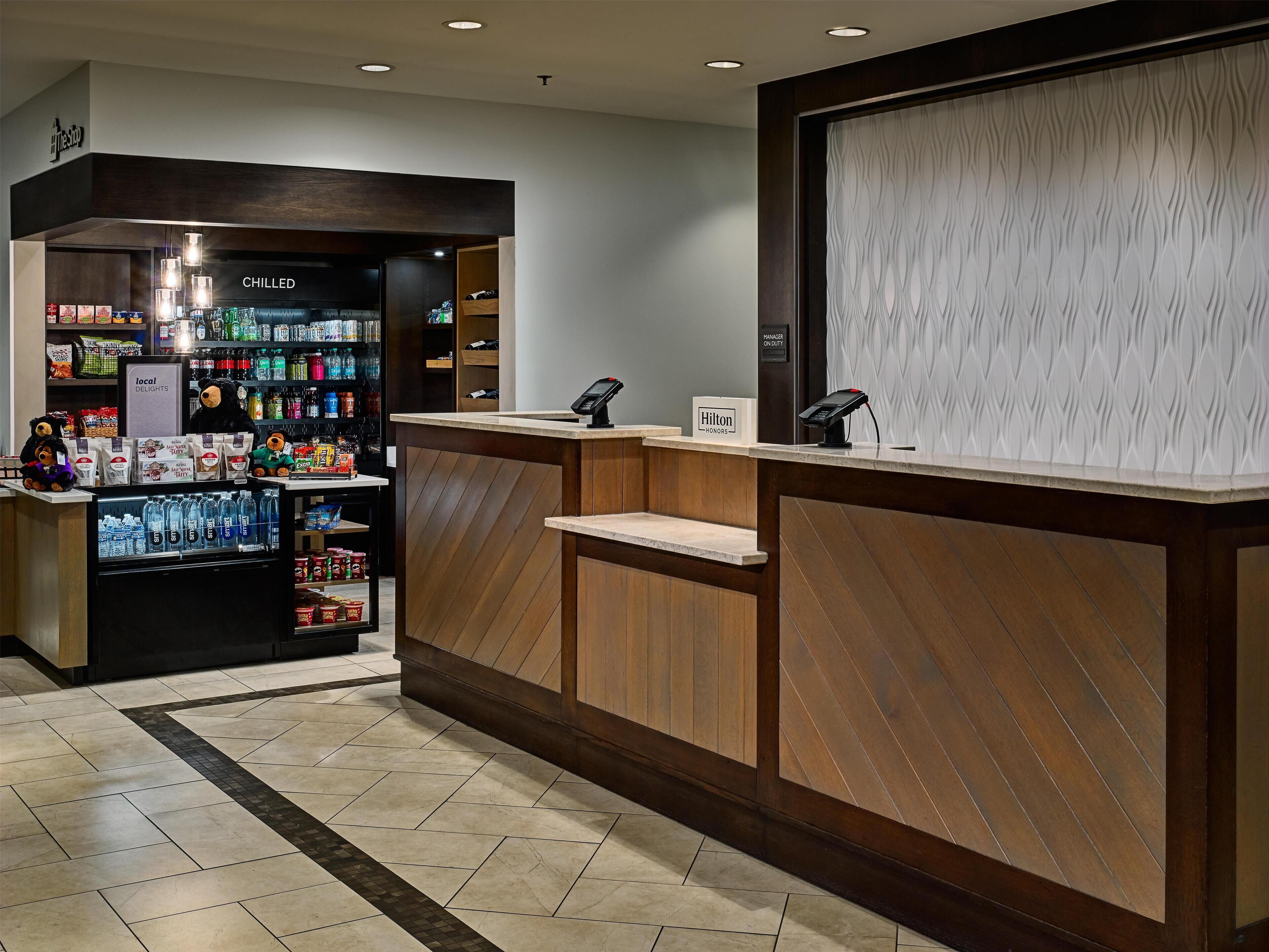 A hotel reception area with a wooden reception desk, a minibar, and a vending machine stocked with snacks and beverages.
