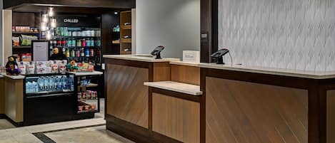 A hotel reception area with a wooden reception desk, a minibar, and a vending machine stocked with snacks and beverages.