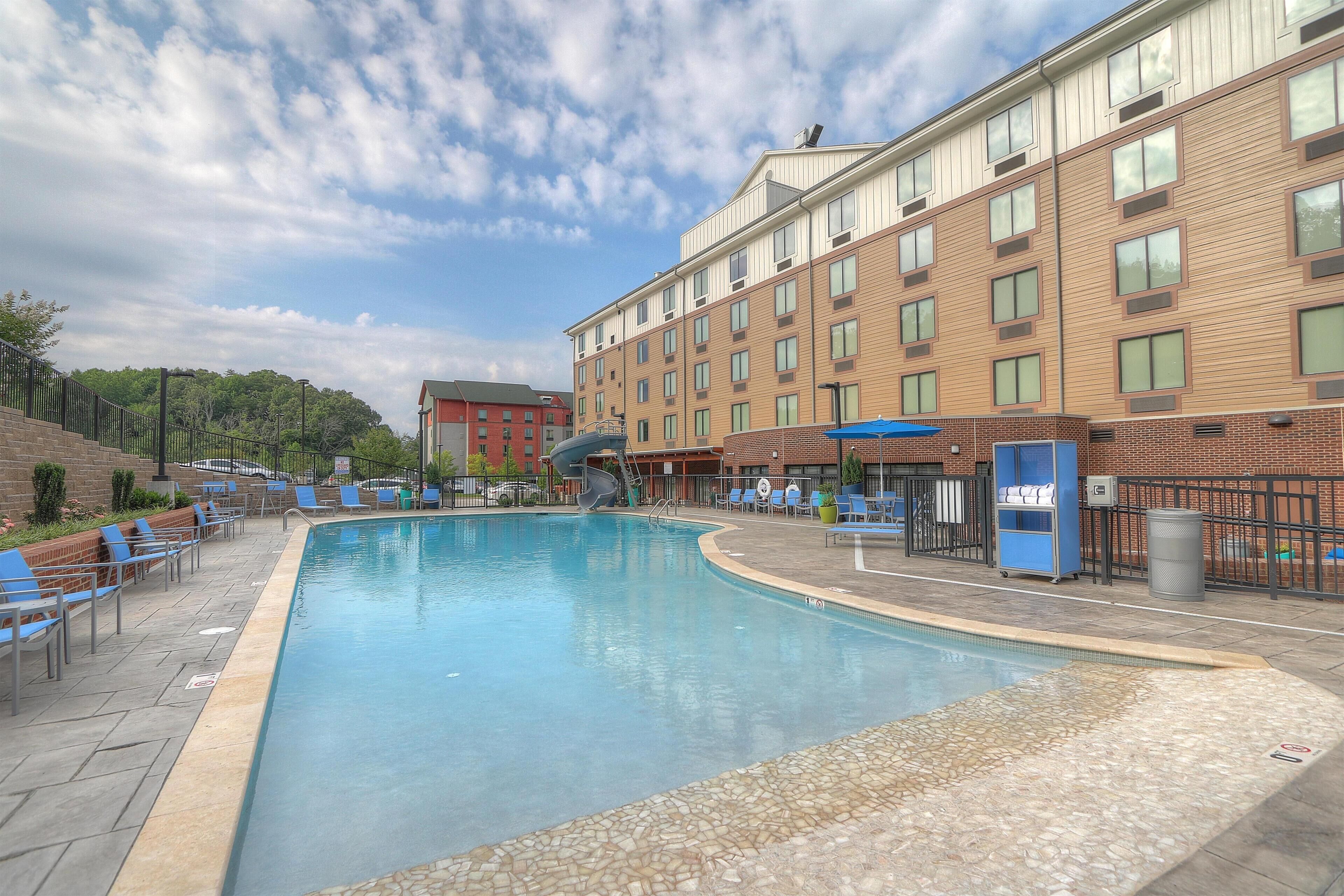 A swimming pool with lounge chairs and a water slide, surrounded by a brick building with multiple windows.