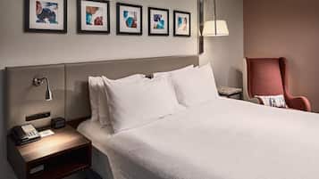 Een hotelkamer met een groot bed, een nachtkastje met een telefoon en een digitale klok, een stoel en kunstwerken aan de muur.